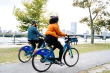 Two bike riders on bike path with city in the background.